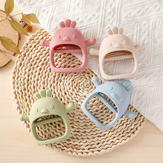 four different colour teething mittens in a chicken design are laying next to each other on a mat.