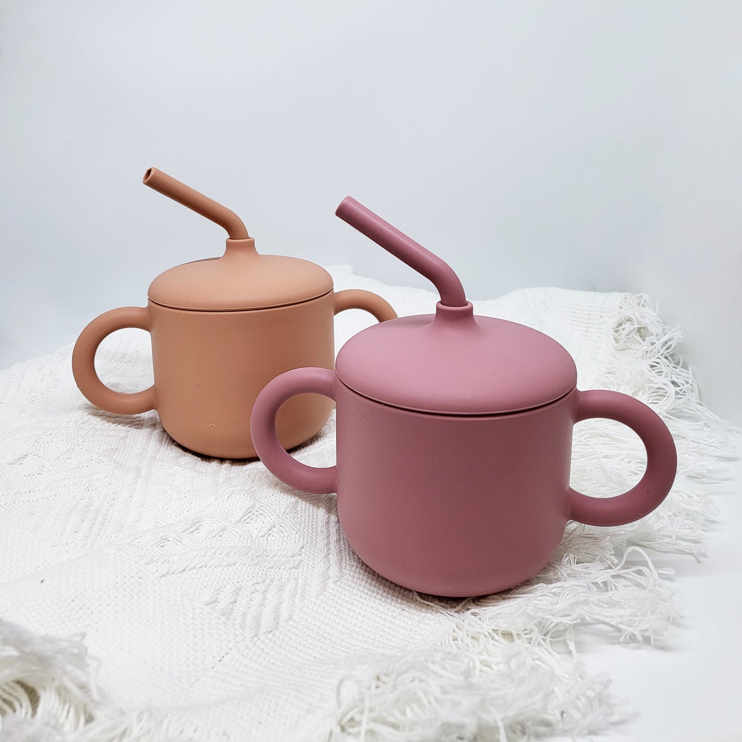 a burnt orange sippy cup is next to a pink sippy cup