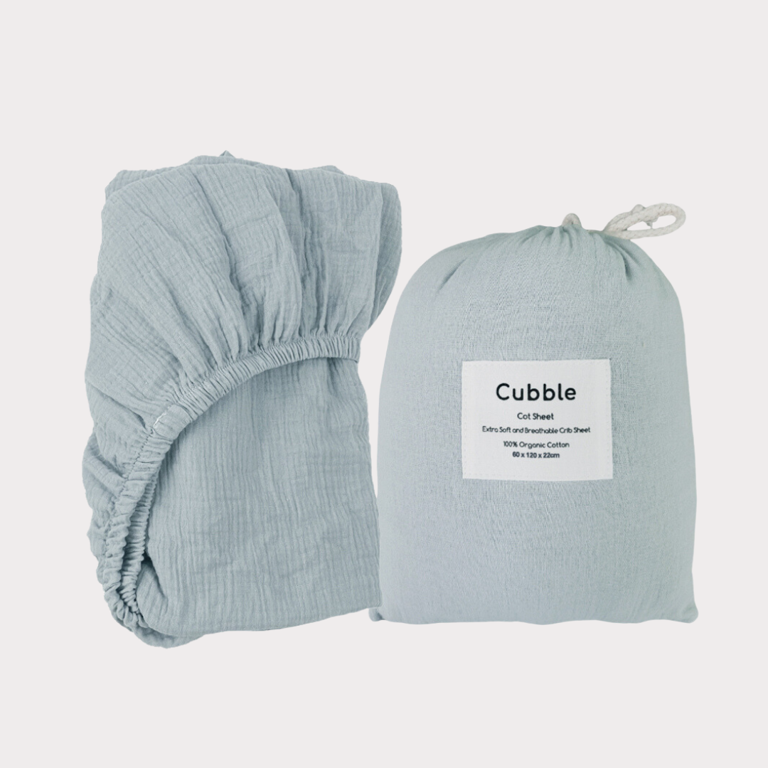 a baby blue cotton crib sheet is folded neatly next to its cotton bag packaging