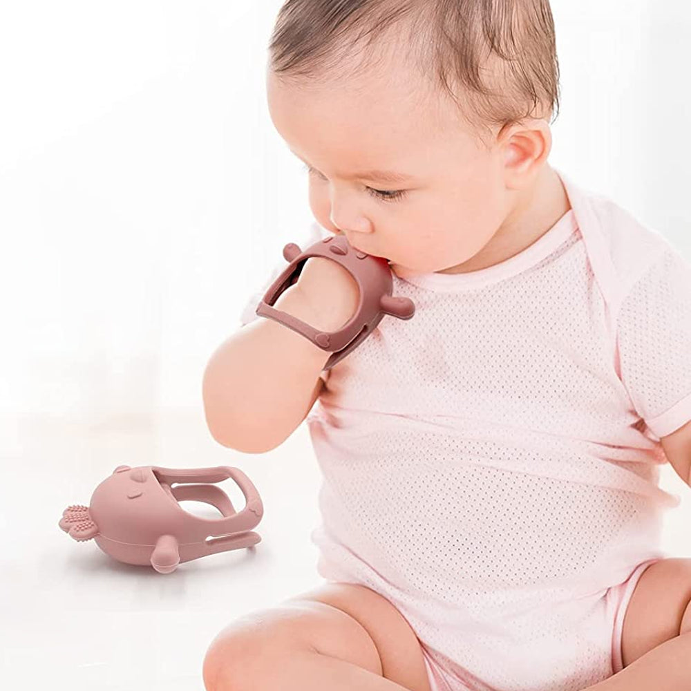 a baby putting a dusty pink chicken teething mitten into her mouth